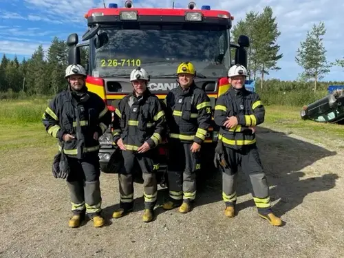 Fyra brandmän står framför brandbil